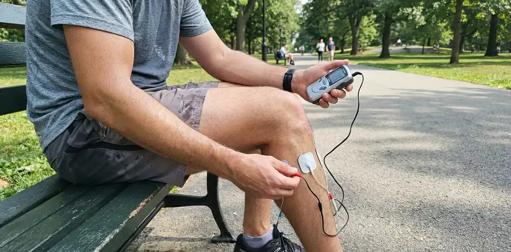 Runner using a portable muscle stimulator on calf after a run